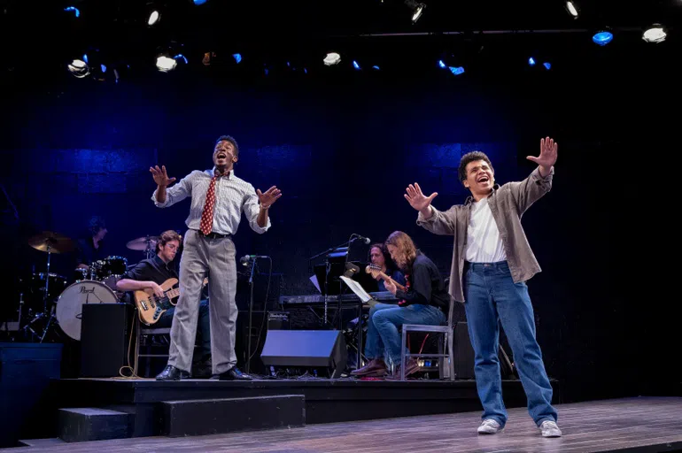 Two performers on stage with music ensemble in the background