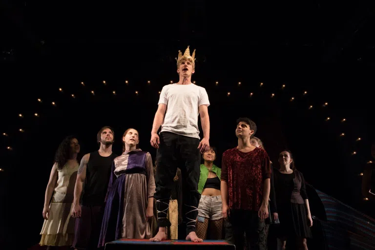 Student performers gathered on stage around an individual in a crown