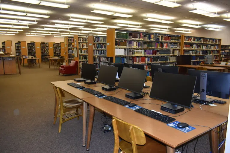 Image of computers, library shelves with books, and desks.  