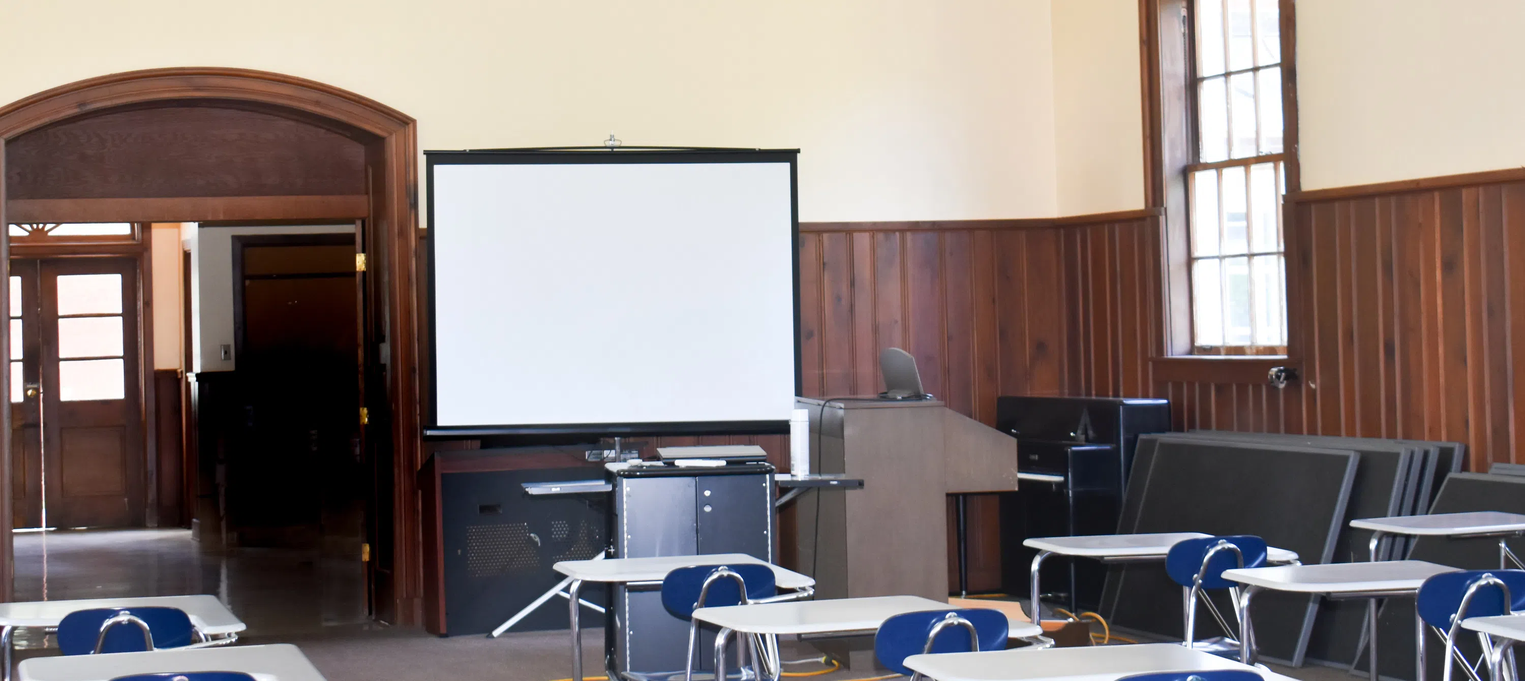 Empty classroom with desks, chairs, and screen inside Suarez Music Building.