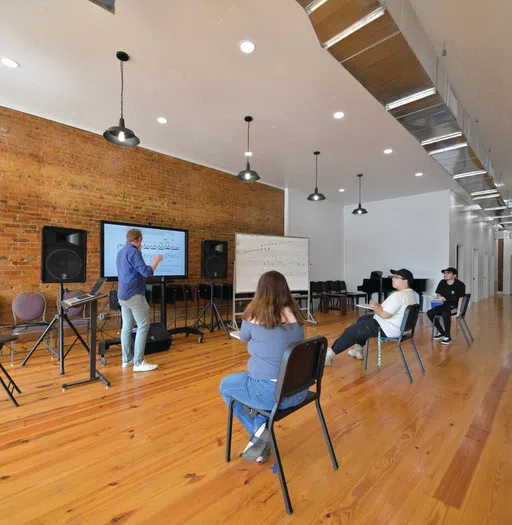 Image of music professor teaching  a small class of students with large screen music technology in the Richard B. Taylor open area space.