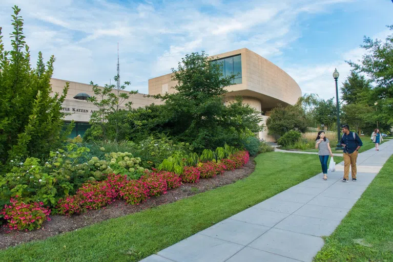 Two students walk along the sidewalk in front of the Katzen Arts Center.