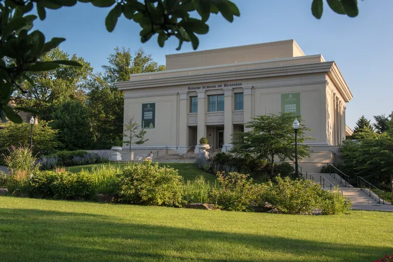 A photo of the Kogod School of Business looking through the trees that surround campus.