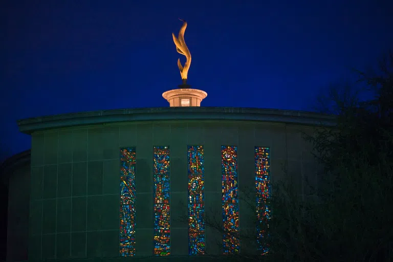 The Kay Spiritual Life Center at night with the metal flame atop illuminated by light.