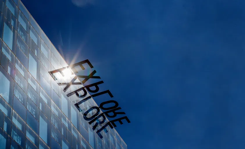 The word "explore" is reflected in the glass of a building as an art installation