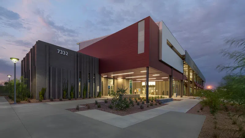 Concrete path and patio with desert landscaping in front of a cinder block and and red metal building at dusk. 