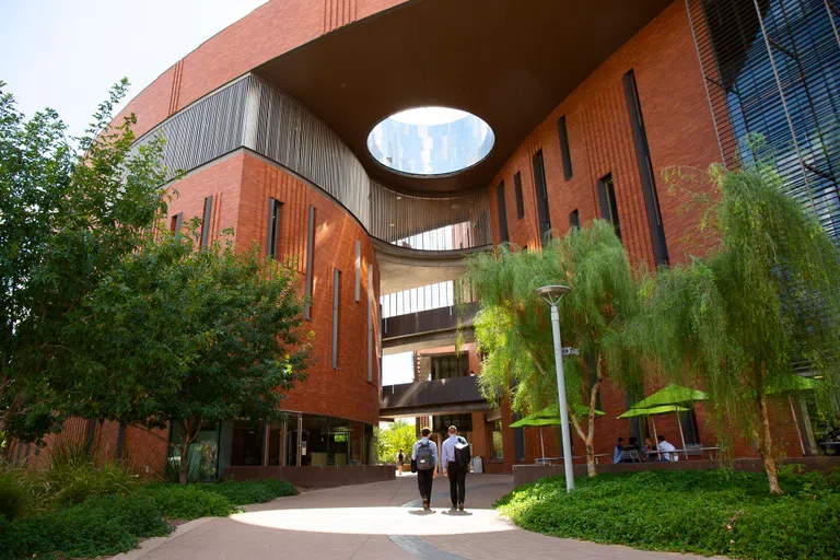 Two men walk toward a four story brick building with outdoor walkways connecting the two sides of the building.