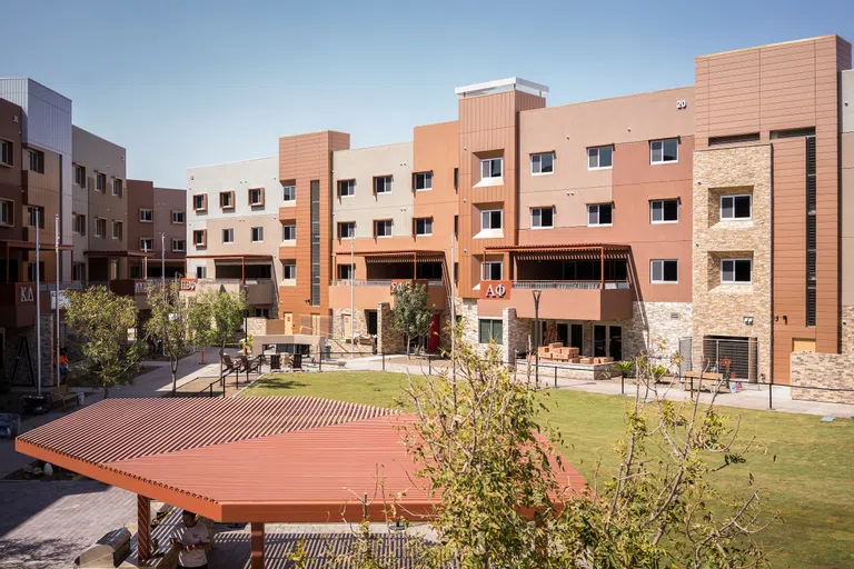 View of covered patio and grassy courtyard surrounded by three and four-story townhouses with Greek letters attached to their balconies. 