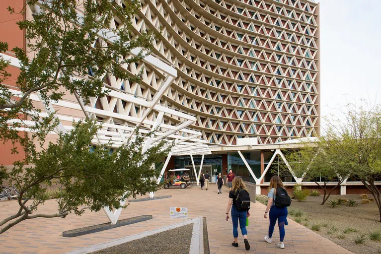 Students walk towads a sixteen-story building with a triangle window pattern.