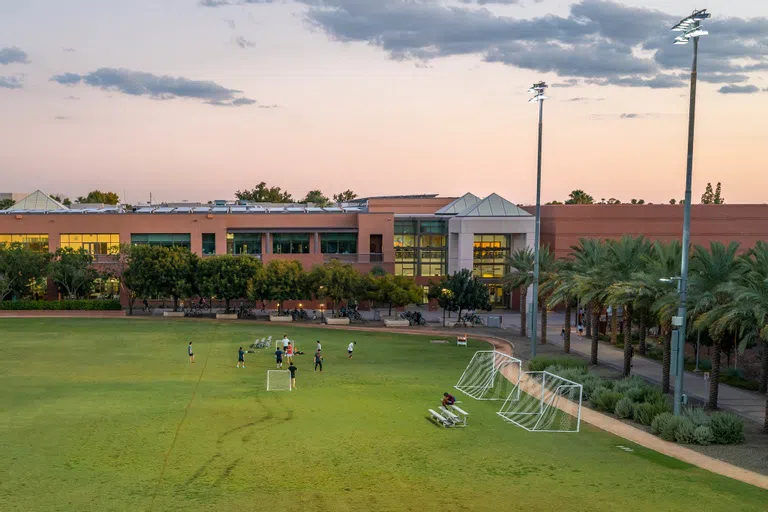 Students practice soccer in a field in front of red brick fitness center. 