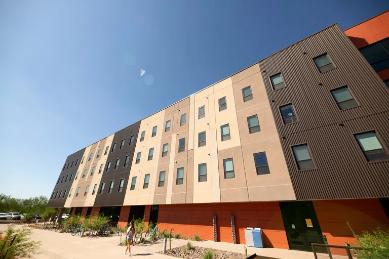 Woman walks on pathway in front of four-story building. 