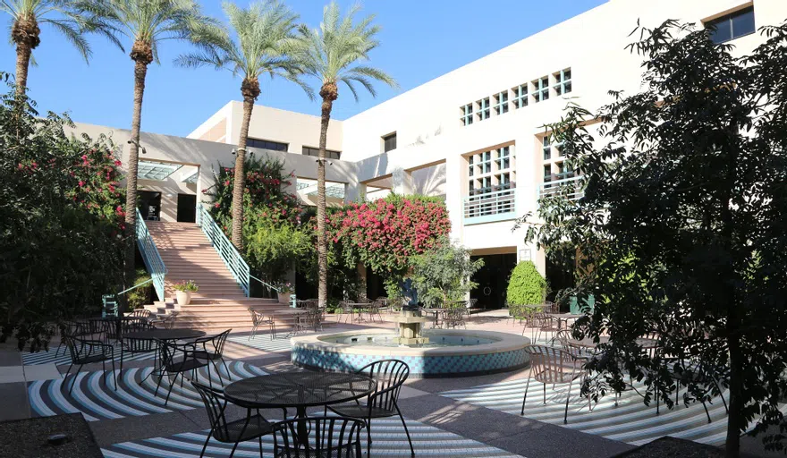 Tables and chairs set up around a central fountain with a staircase to the second floor in the background.