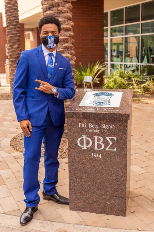 A Phi Beta Sigma representative stands next to his society's plaque. 