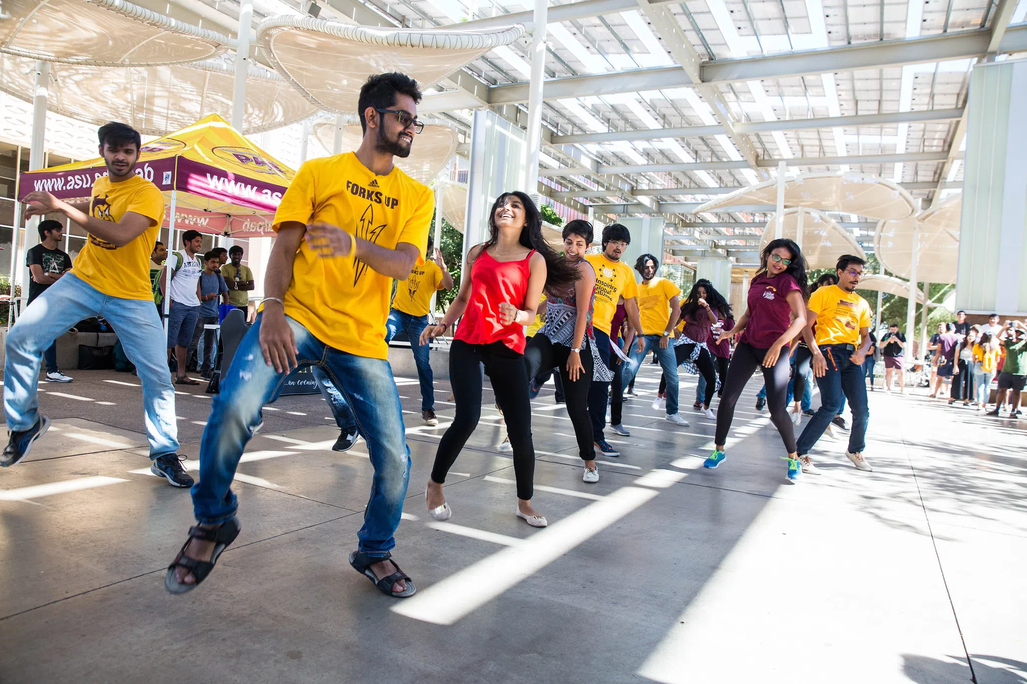 15 people in three rows perform a dance outside building.