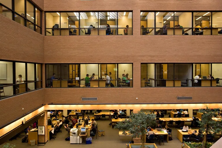 View of students studying alone and in small groups through windows in interior courtyard of building.