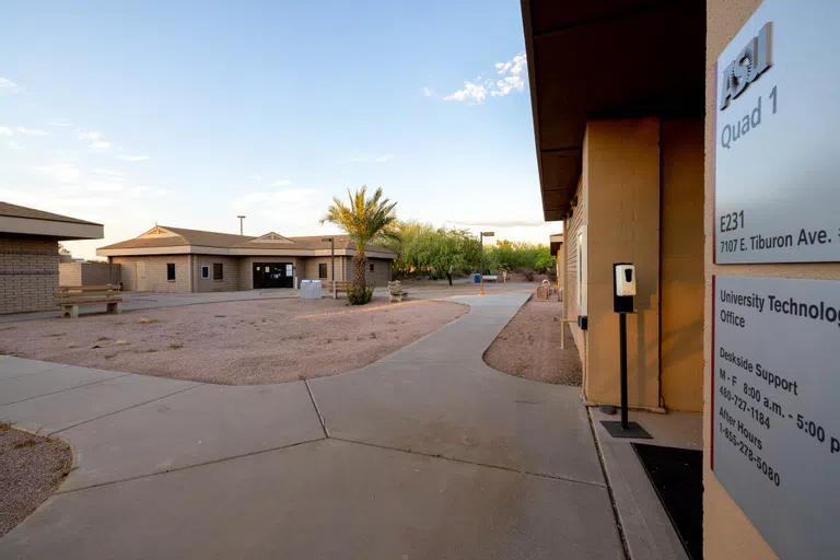 A desert rock courtyard between four brick buildings with the nearest most building featuring a metal sign that reads "Quad 1". 