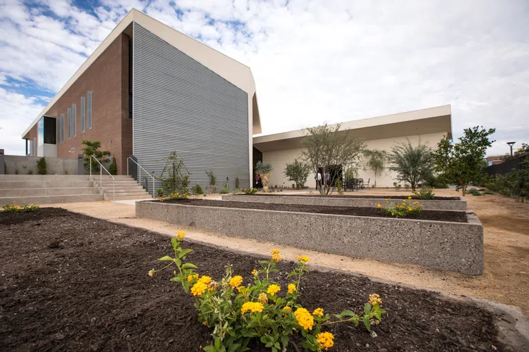 Yellow flowers are freshly planted in concrete raised flower beds in front of metal and brick building.