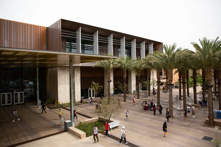 People walk around a palm tree-lined courtyard in front of a copper building.