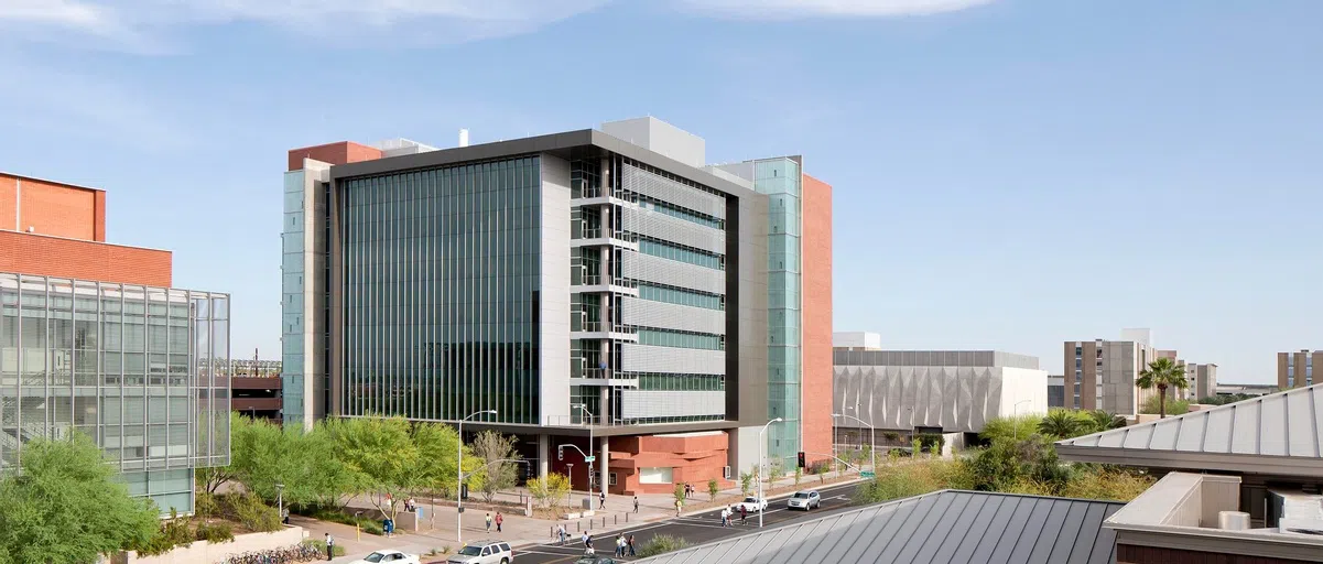 Pedestrians and cars go past seven-story brick, glass and metal building. 