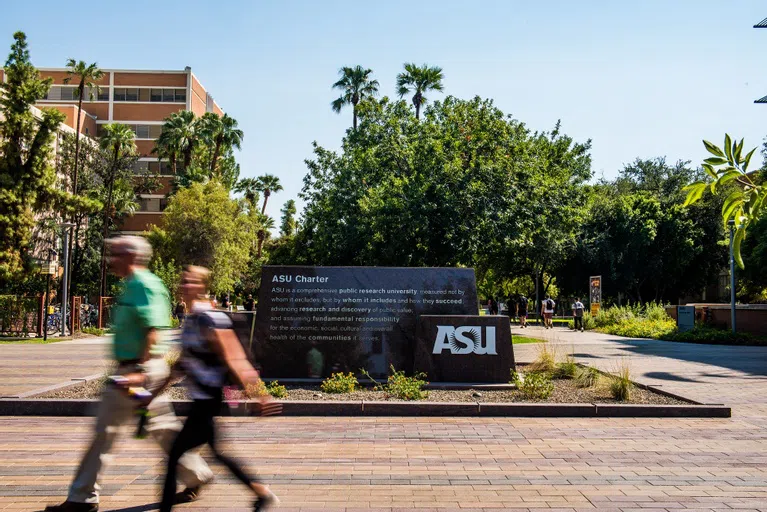 Two people walk by a stone sign with the ASU Charter inlaid on the side of it.