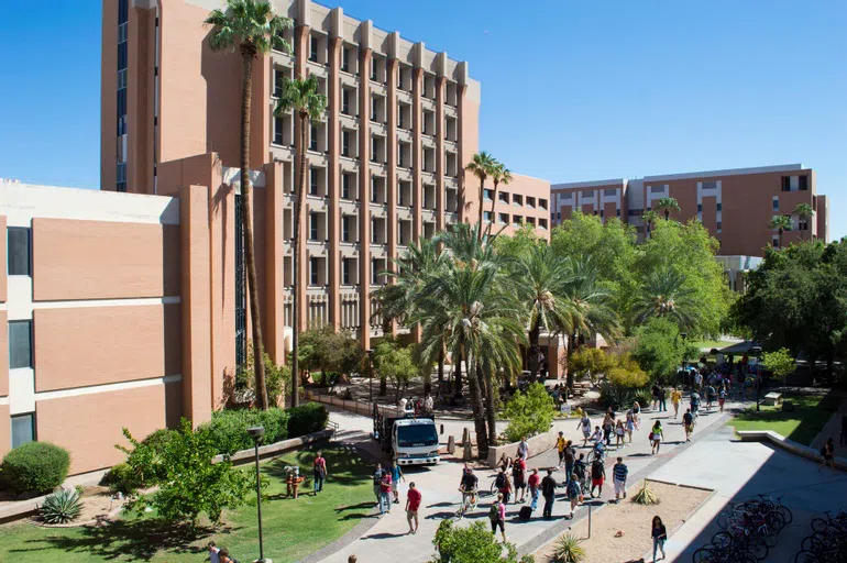 Students walk past an eight-story brick building.