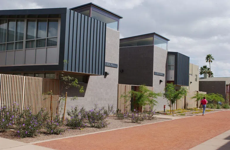 A gravel walkway and desert landscaping are in front of two cinderblock buildings with gray meal siding on the second floor.