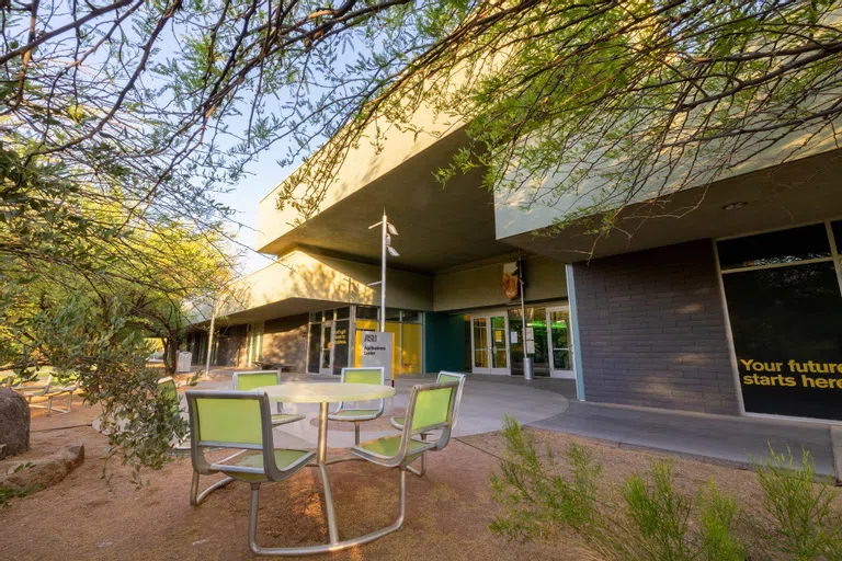 Tree branches hang over a green, outside table in front of the Agribusiness Center building.