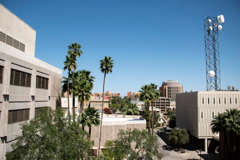 View of multiple concrete buildings, with trees and vegetation around. The building on the right has a large antenna on the roof. 