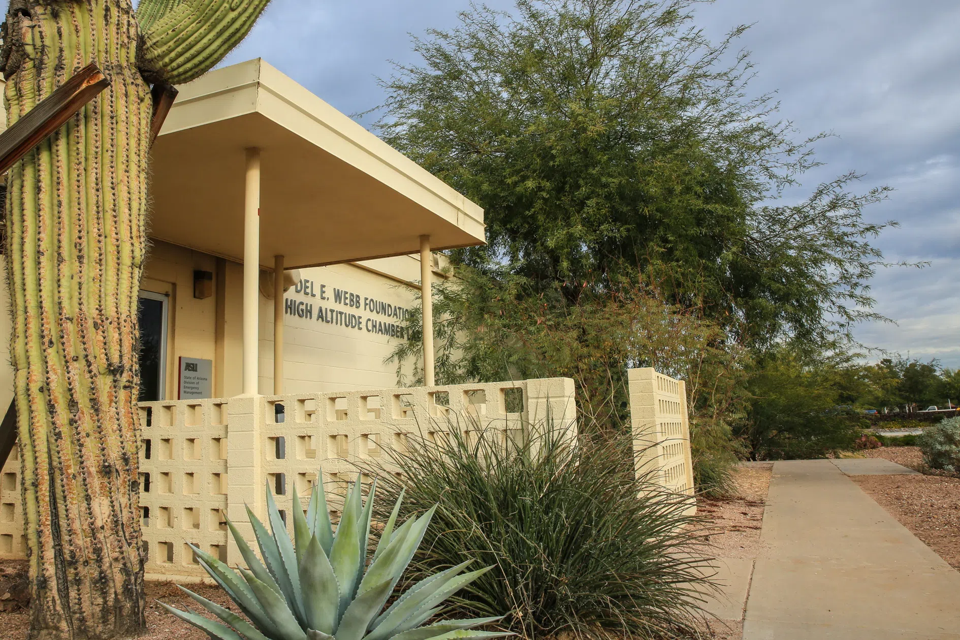 Saguaro and desert plants are in front of light yellow cinderblock building labeled Del E. Webb Foundation High Altitude Chamber Lab