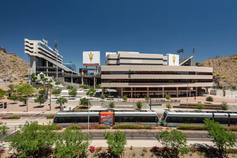 Veterans Way street and a light rail train in front of  Sun Devil Stadium.