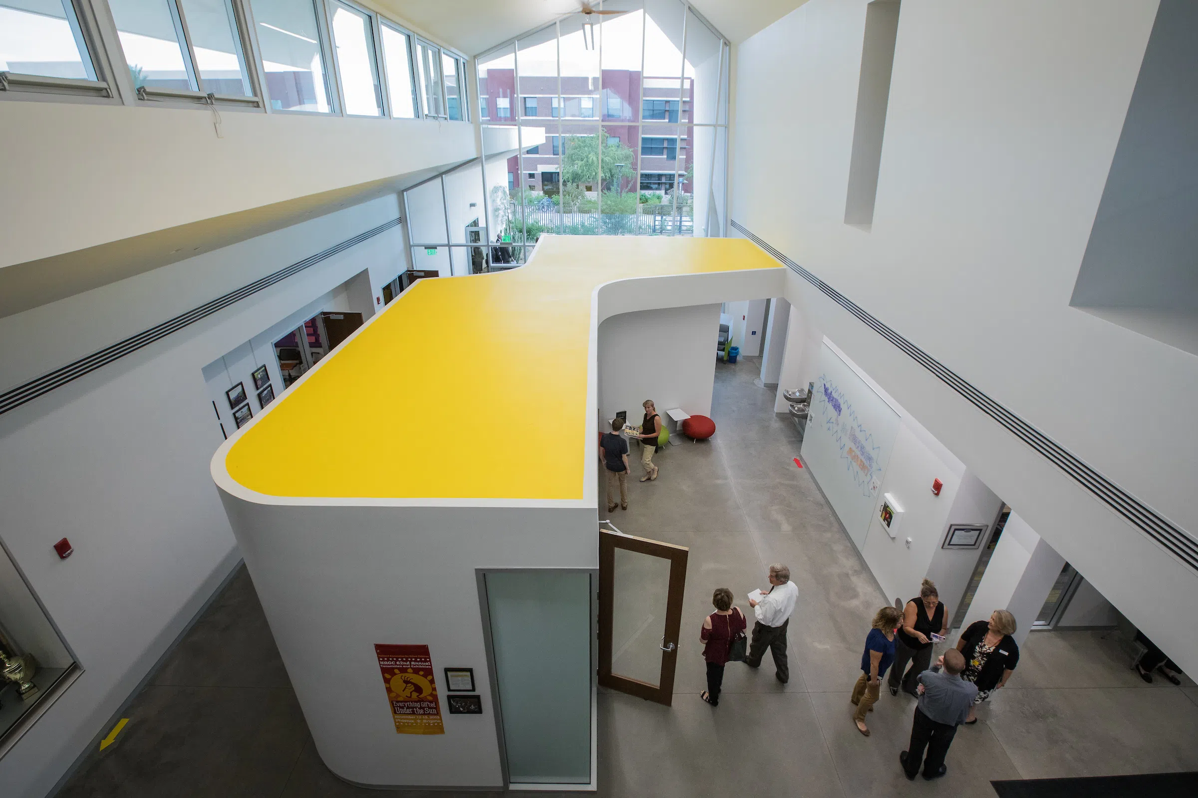 Second-floor view of several people walking around main hallway inside building. 