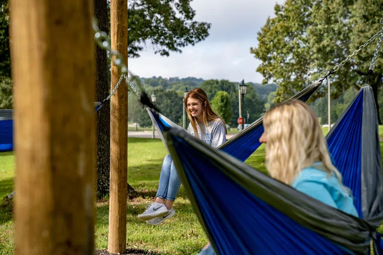 Two students sit in hammocks outside