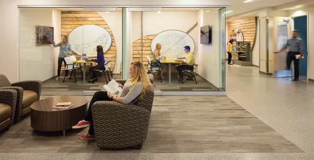 A study space in the Biology building. Students sit in the foreground studying while other students sit in study rooms in the background.