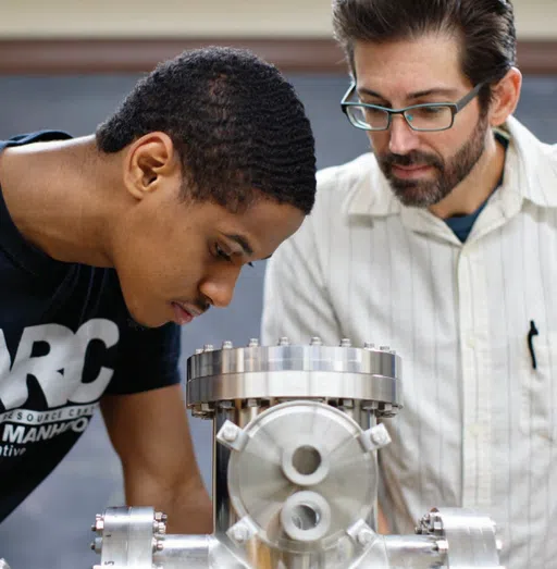 A professor watches as a student looks over equipment.