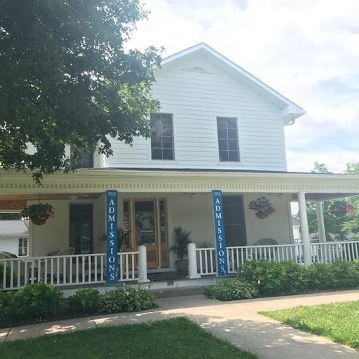 Large, white two-story house with welcoming front porch. Blue Admissions banners hang on porch columns.