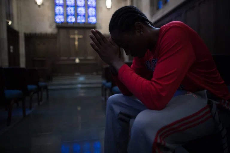 Student sits in quiet prayer or reflection in the Danforth Chapel. Stained glass windows and a large cross are on the wall behind him.