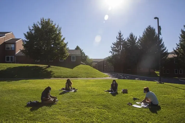 Students sitting outside on the grass near the apartment buidlings