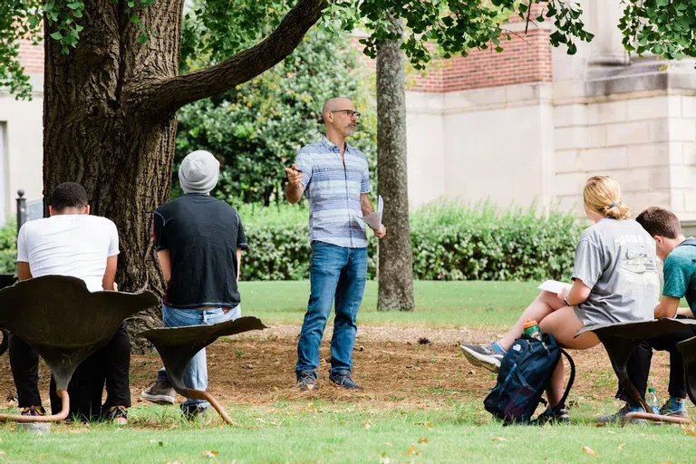 Photo of a faculty member teaching a class in the outdoor classroom under a Ginkgo tree