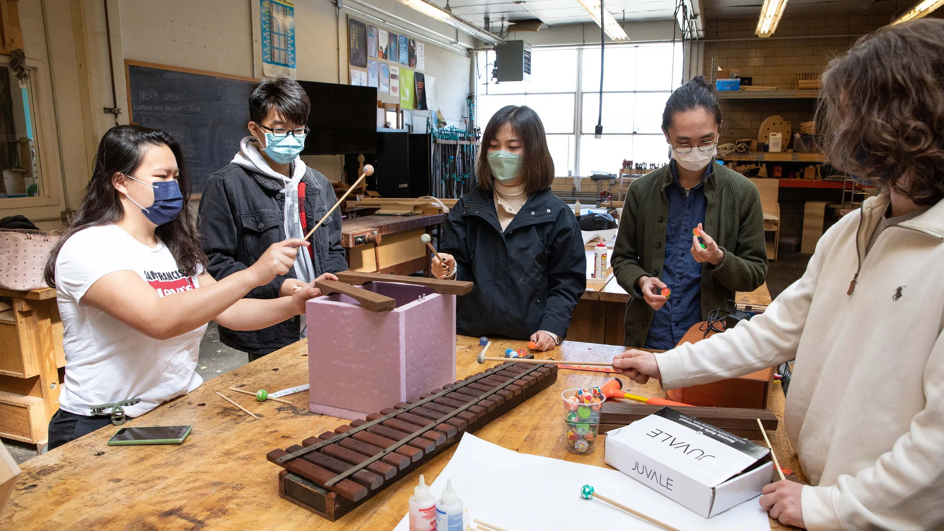 Five students play with hand-made marimas around a wooden table in the Bench Room.