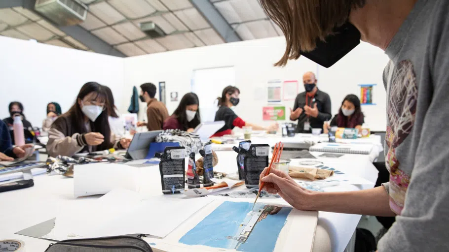 A group of students work on watercolor paintings around a table. 