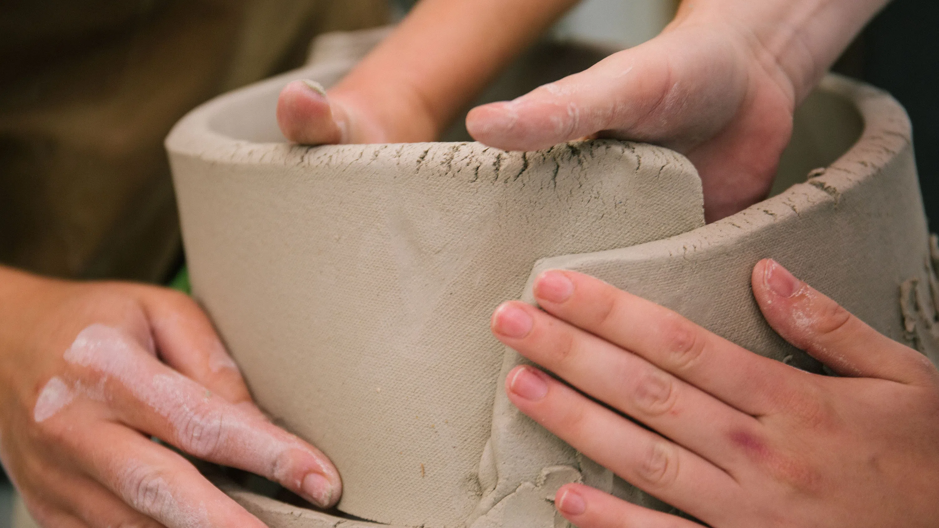 Two sets of hands create circular forms from slab-rolled clay.