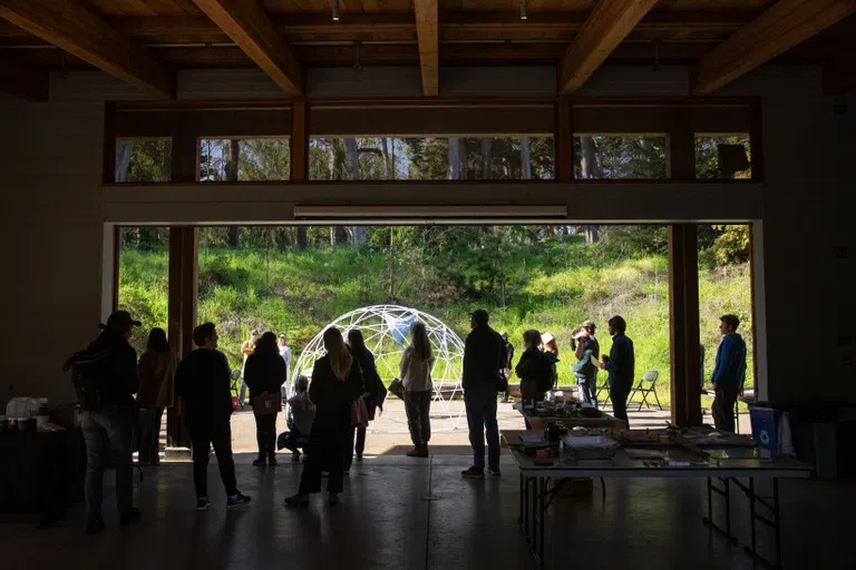 A group of people stand backlit looking outside at a domed structure they constructed.