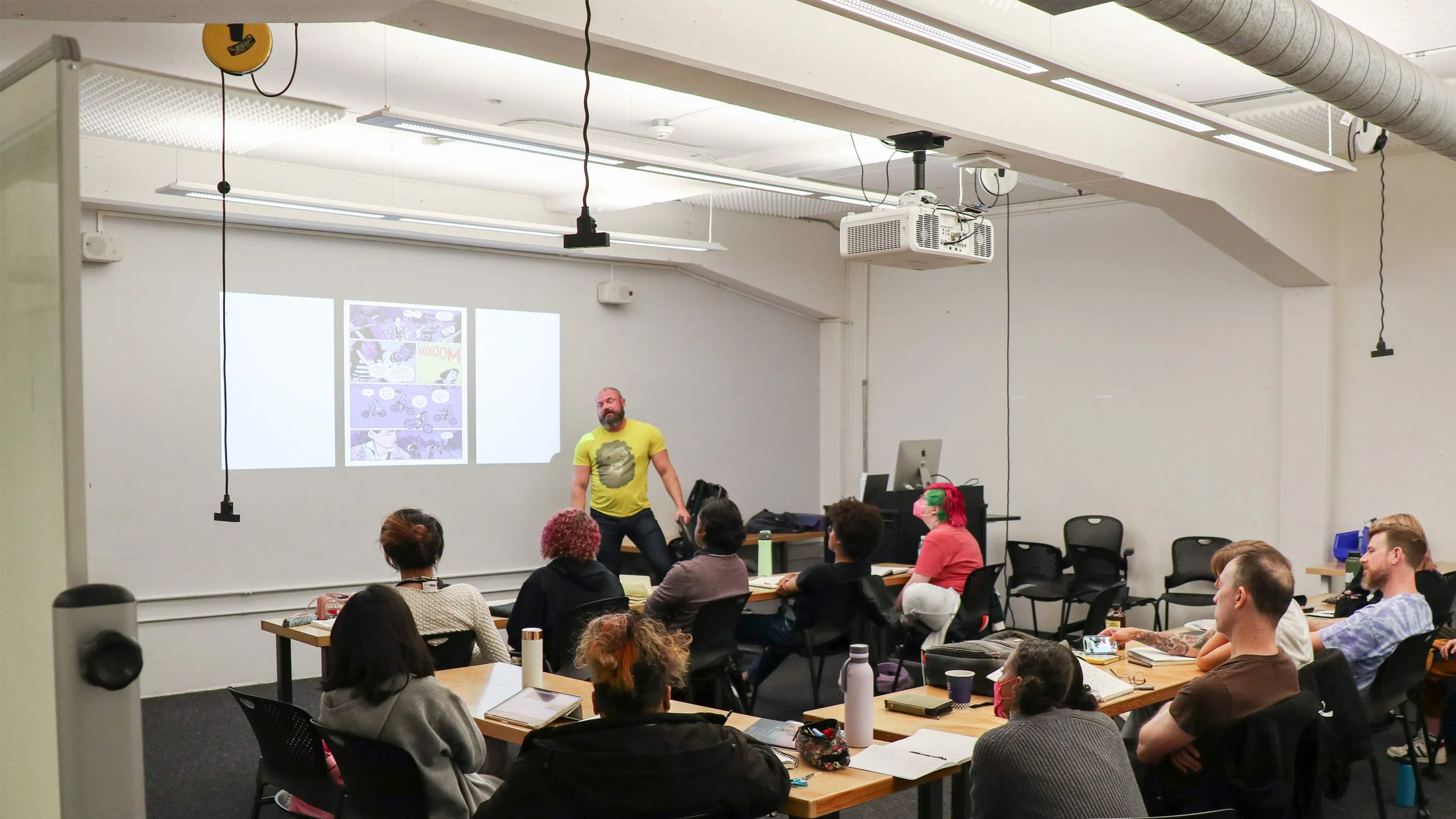 Teacher in a yellow t-shirt standing in front of a classroom of students.