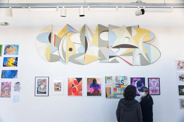 Two students look at illustration work pinned to a white wall.