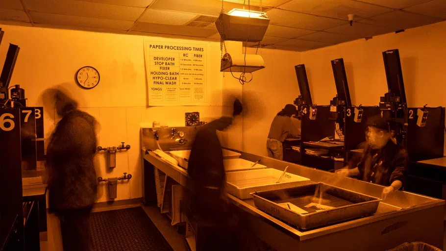 Four students work at various stations in the darkroom, two at enlargers and two washing prints.