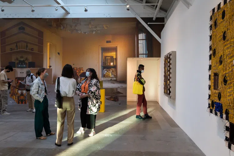 Three CCA students converse in the Wattis’ warehouse space with Josh Faught’s large-scale weavings on view.