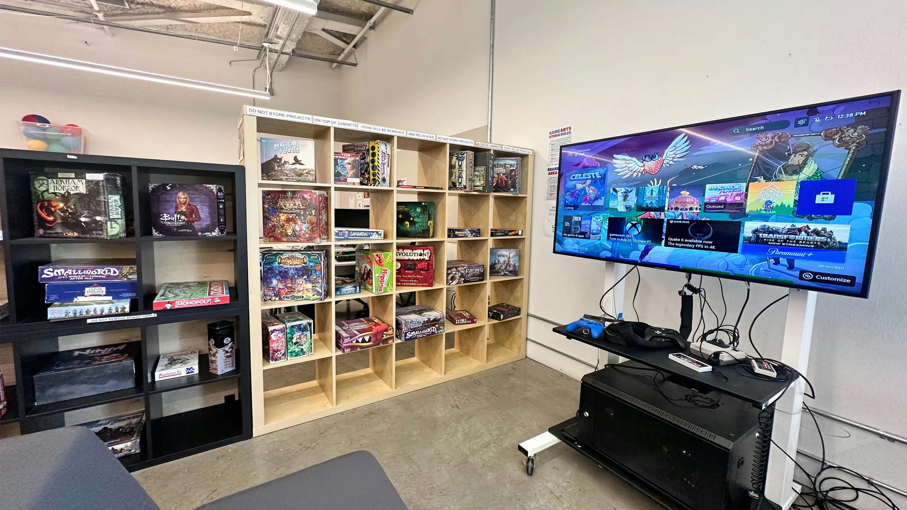 A room with a TV, computer, and game shelf.