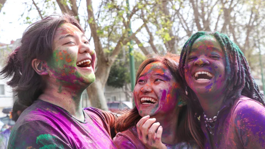 Three students embrace, their faces covered in colorful dust.