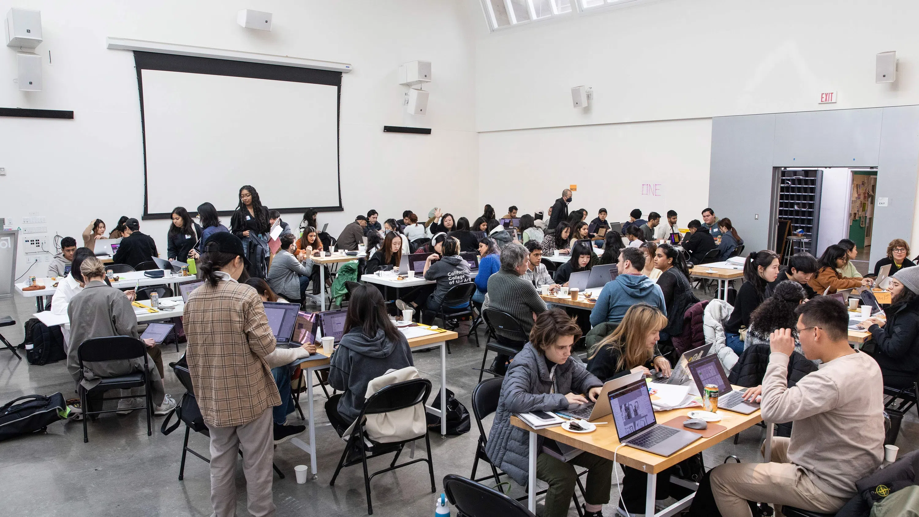 Dozens of students with their laptops sitting in groups. 