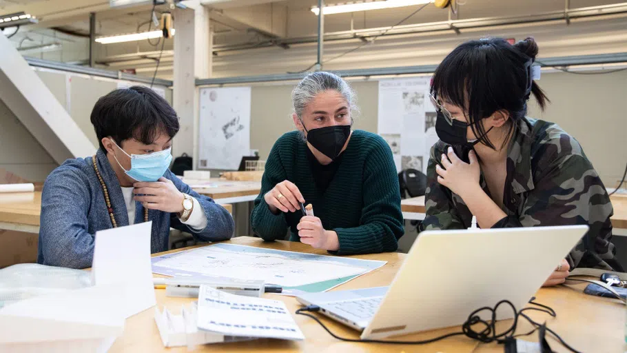 Two students look at an architectural drawing with a faculty member.